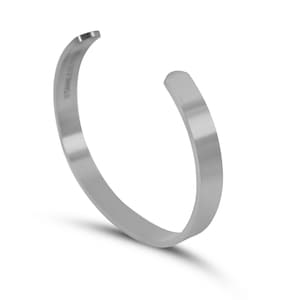 Puede incluir: Un brazalete de metal plateado con un acabado liso y pulido.