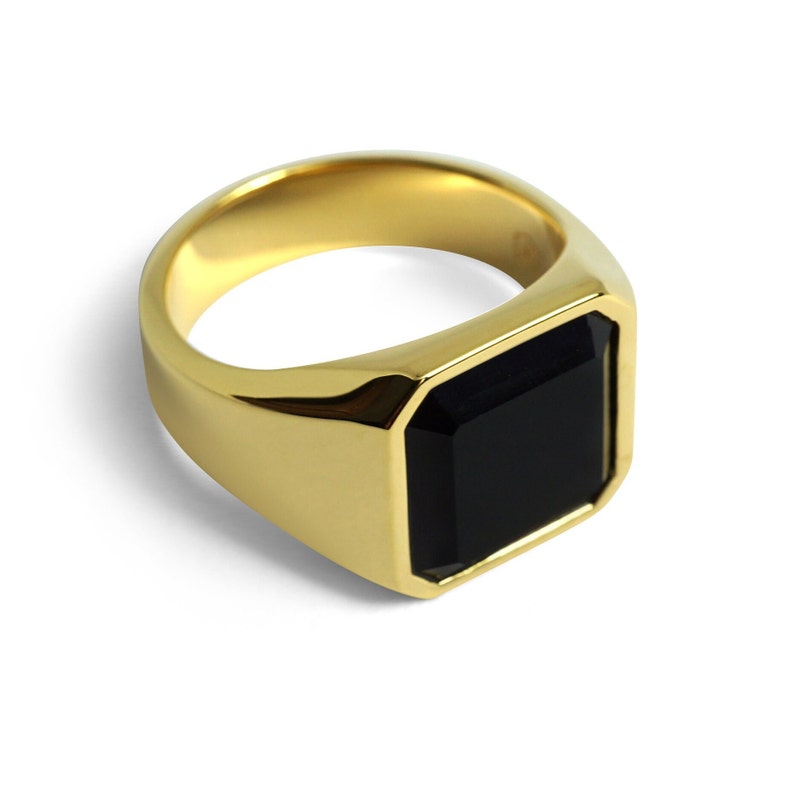 Seitliche Ansicht eines goldenen Herrenrings mit quadratischer Form. Der Kontrast zwischen Onyx und Gold betont die klare Linienführung.