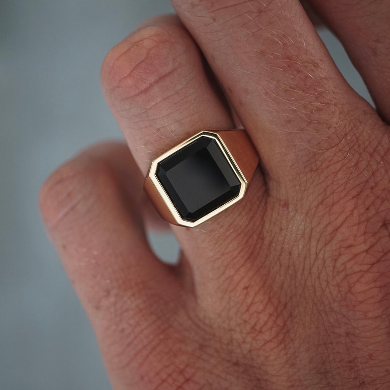 Nahaufnahme des schwarzen Onyx-Steins in goldener Fassung. Die polierte Oberfläche spiegelt Licht und Luxus zugleich wider.