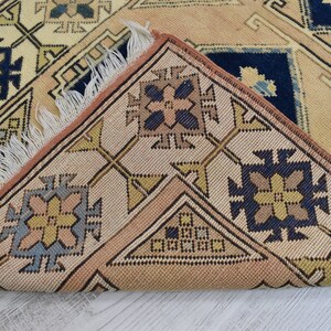 May include: Close-up of a beige and brown patterned rug with a fringe border. The rug features geometric designs in shades of blue, yellow, and brown.