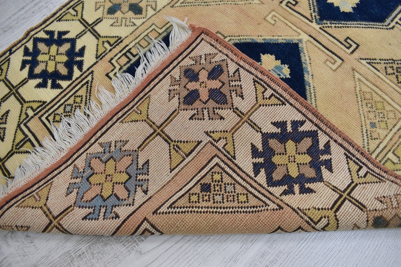 May include: Close-up of a beige and brown patterned rug with a fringe border. The rug features geometric designs in shades of blue, yellow, and brown.