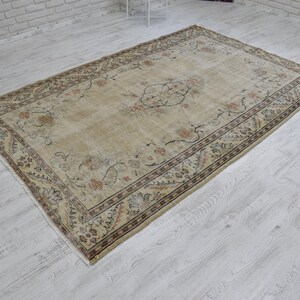 May include: A beige vintage rug with a floral pattern and a dark brown border. The rug has a worn and faded look, giving it a rustic and antique feel.