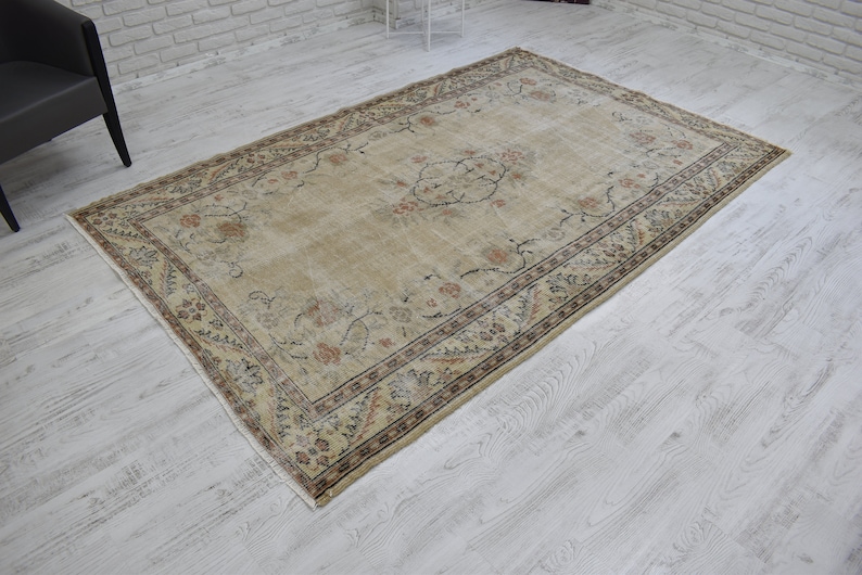 May include: A beige vintage rug with a floral pattern and a dark brown border. The rug has a worn and faded look, giving it a rustic and antique feel.