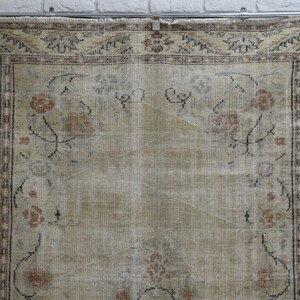 May include: A vintage rug with a cream background and a floral pattern in shades of brown, pink, and blue. The rug has a border with a geometric design.