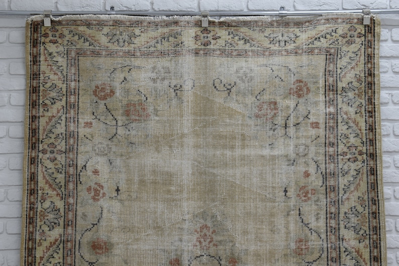 May include: A vintage rug with a cream background and a floral pattern in shades of brown, pink, and blue. The rug has a border with a geometric design.
