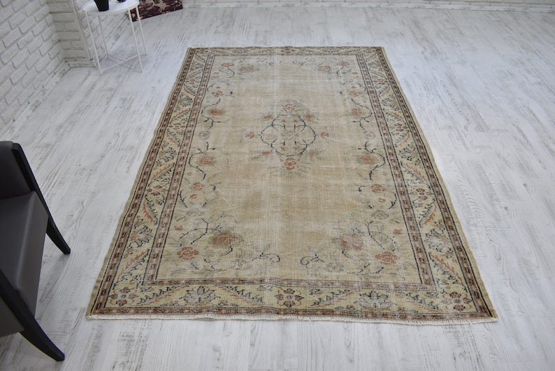 May include: A vintage rug with a beige background and a floral pattern in shades of brown, pink, and black. The rug has a border with a repeating pattern.