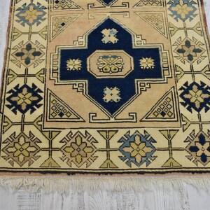 May include: A beige and blue patterned rug with a central medallion and a fringe border. The rug has a traditional design with geometric shapes and floral motifs.