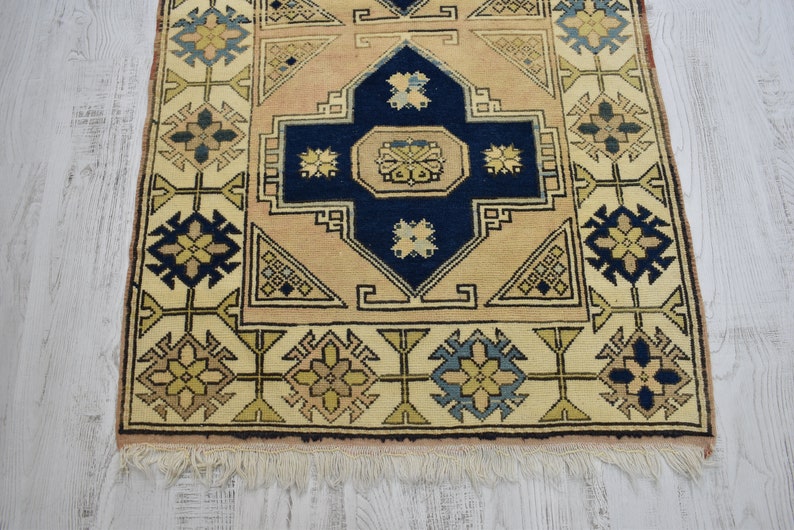 May include: A beige and blue patterned rug with a central medallion and a fringe border. The rug has a traditional design with geometric shapes and floral motifs.