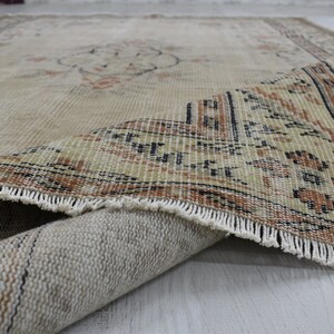 May include: A beige rug with a brown and black geometric pattern along the edge. The rug is folded in half, showing the underside of the rug.