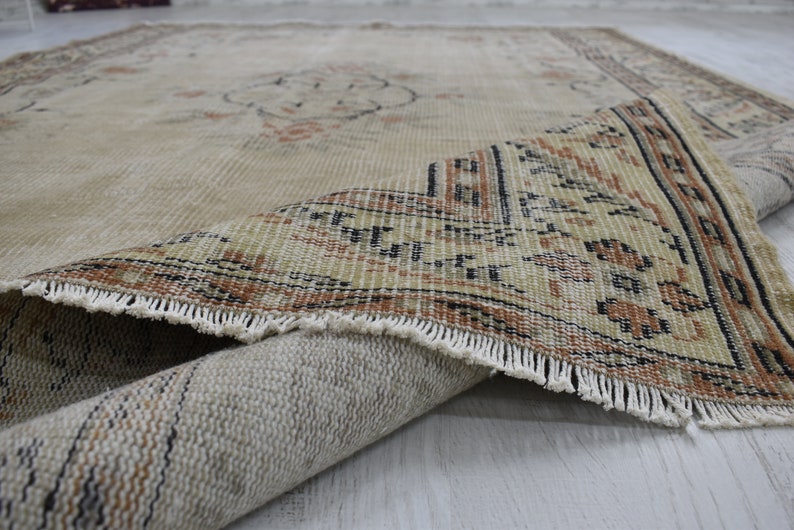 May include: A beige rug with a brown and black geometric pattern along the edge. The rug is folded in half, showing the underside of the rug.