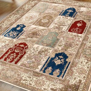 May include: A cream-colored rug with a patchwork design featuring blue, red, and green accents. The rug has a detailed floral pattern and a border with intricate designs.