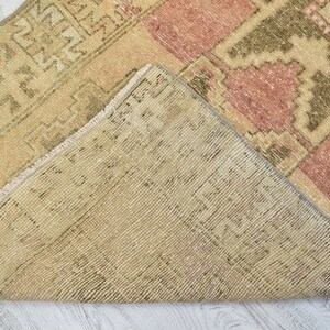 Puede incluir: Una alfombra vintage con un patr&oacute;n geom&eacute;trico en tonos beige, rosa y verde. La alfombra tiene un borde de flecos y est&aacute; tejida con una t&eacute;cnica tradicional.
