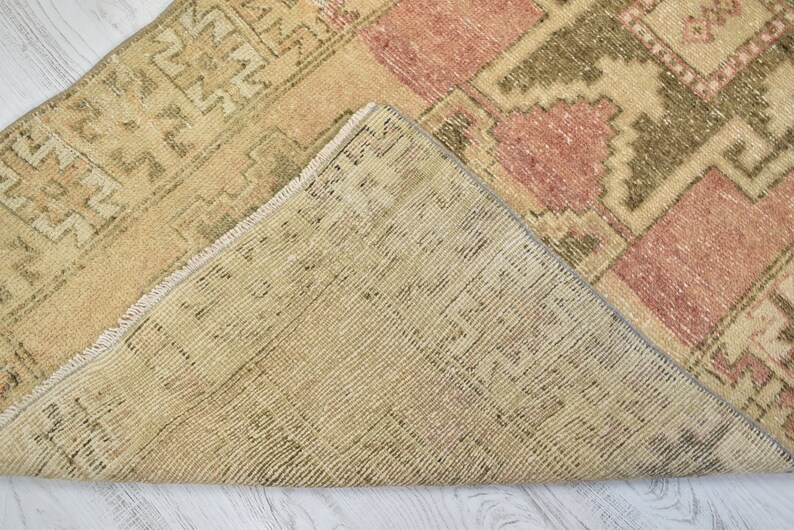 Puede incluir: Una alfombra vintage con un patr&oacute;n geom&eacute;trico en tonos beige, rosa y verde. La alfombra tiene un borde de flecos y est&aacute; tejida con una t&eacute;cnica tradicional.