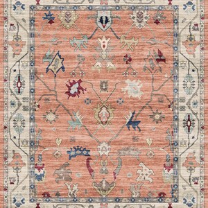 May include: A peach-colored rug with a traditional Persian design. The rug has a cream-colored border with intricate floral patterns. The center of the rug features a repeating pattern of stylized flowers and leaves.