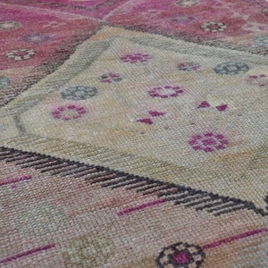 K&ouml;nnte beinhalten: Ein Vintage-Teppich in Rosa und Beige. Der Teppich hat ein rautenf&ouml;rmiges Muster mit filigranen Details in Rosa-, Beige- und Schwarzt&ouml;nen.