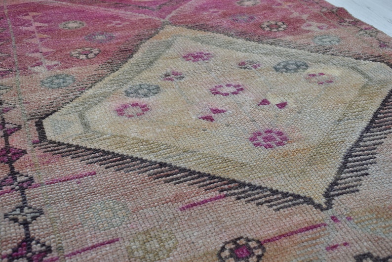 K&ouml;nnte beinhalten: Ein Vintage-Teppich in Rosa und Beige. Der Teppich hat ein rautenf&ouml;rmiges Muster mit filigranen Details in Rosa-, Beige- und Schwarzt&ouml;nen.