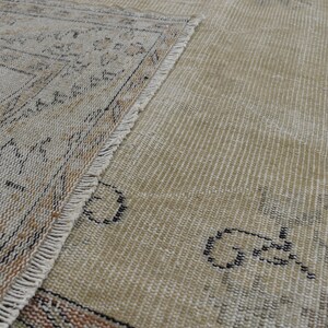May include: Close-up of a beige rug with a fringe border. The rug has a woven pattern with black and brown accents.