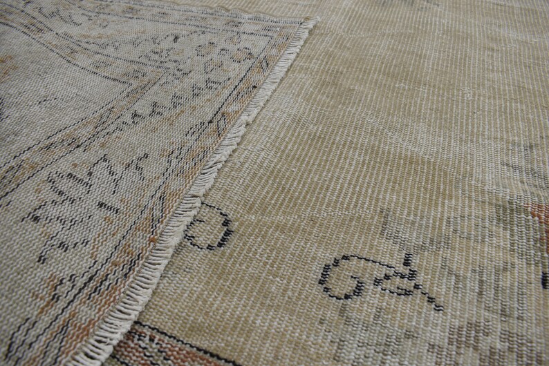 May include: Close-up of a beige rug with a fringe border. The rug has a woven pattern with black and brown accents.