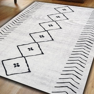 May include: A white rug with a black geometric pattern. The pattern features a series of diamonds with a small flower design inside each diamond. The rug has a chevron border.