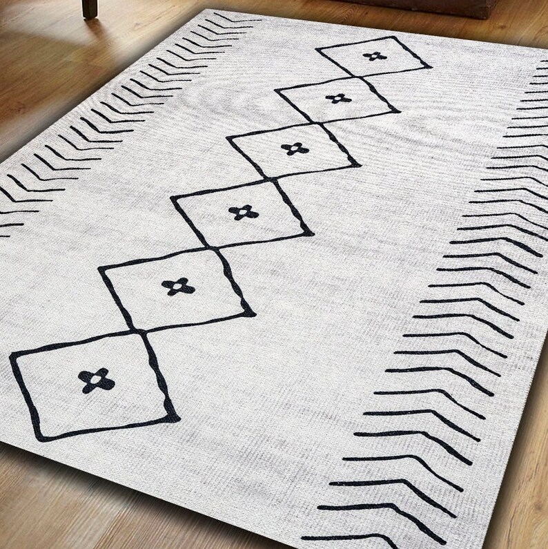 May include: A white rug with a black geometric pattern. The pattern features a series of diamonds with a small flower design inside each diamond. The rug has a chevron border.