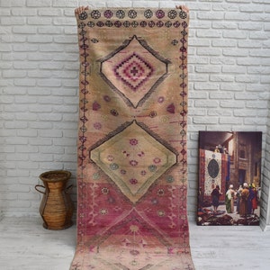 K&ouml;nnte beinhalten: Ein Vintage-Teppich in Rosa und Beige mit einem Rautenmuster. Der Teppich hat unten einen Fransen und ist aus Wolle.
