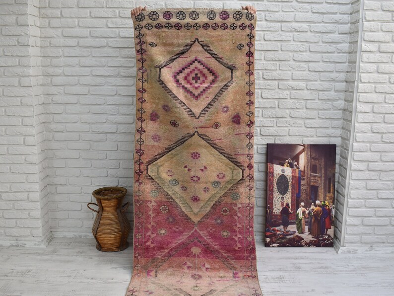 K&ouml;nnte beinhalten: Ein Vintage-Teppich in Rosa und Beige mit einem Rautenmuster. Der Teppich hat unten einen Fransen und ist aus Wolle.