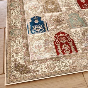 May include: A cream-colored rug with a patterned border and a central design featuring a patchwork of different colored squares. The squares feature intricate floral and geometric designs in shades of red, blue, green, and gold.