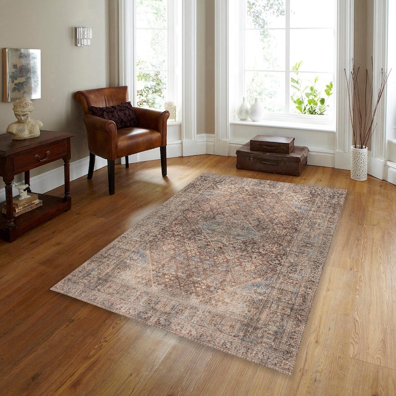 May include: A brown and beige patterned area rug with a faded, vintage look. The rug has a geometric design with a central diamond shape.