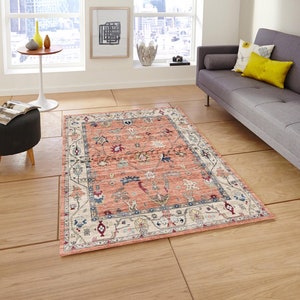 May include: A peach-colored rug with a cream-colored border and intricate floral and geometric patterns in shades of blue, red, and cream.