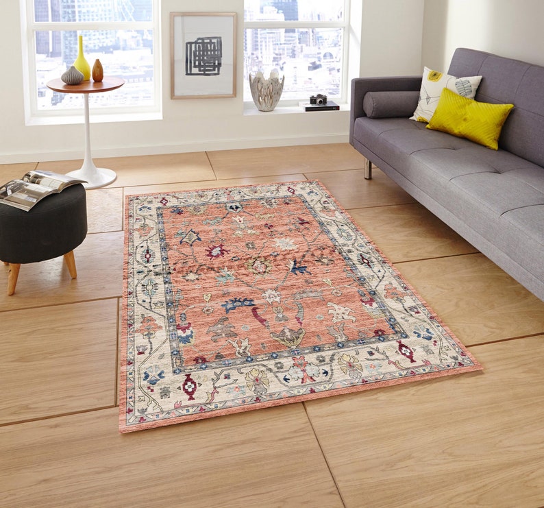 May include: A peach-colored rug with a cream-colored border and intricate floral and geometric patterns in shades of blue, red, and cream.
