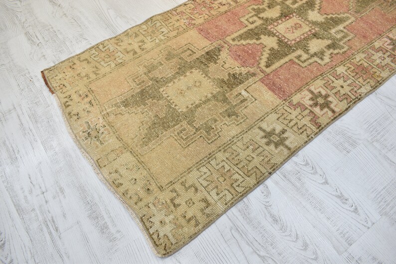 Puede incluir: Una alfombra turca vintage con un patr&oacute;n geom&eacute;trico en tonos beige, rosa y verde. La alfombra tiene un aspecto desgastado y es perfecta para a&ntilde;adir un toque de estilo bohemio a tu hogar.