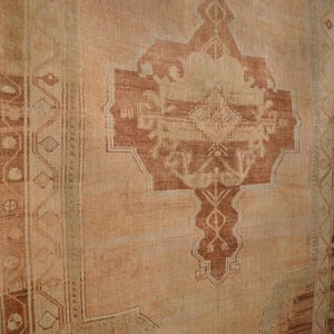 May include: A vintage rug with a central geometric design in shades of brown and beige. The rug has a distressed appearance, with faded colors and visible wear. The border features a repeating pattern, adding to the rug's traditional aesthetic.