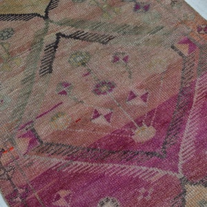K&ouml;nnte beinhalten: Ein Vintage-Teppich in einem rosafarbenen, beigefarbenen und grauen Farbschema. Der Teppich hat ein geometrisches Muster mit floralen Motiven.