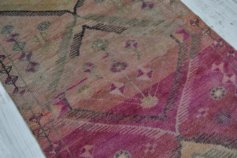 K&ouml;nnte beinhalten: Ein Vintage-Teppich in einem rosafarbenen, beigefarbenen und grauen Farbschema. Der Teppich hat ein geometrisches Muster mit floralen Motiven.