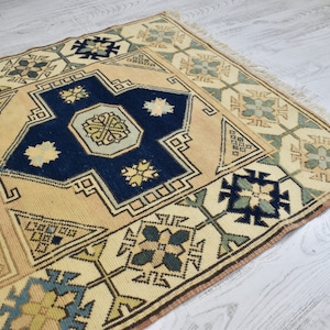 May include: A vintage rug with a cream background and intricate blue, green, and yellow geometric patterns. The rug has a fringed edge.