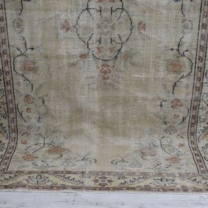 May include: A vintage rug with a beige background and a floral pattern in shades of brown, black, and cream. The rug has a fringed edge.