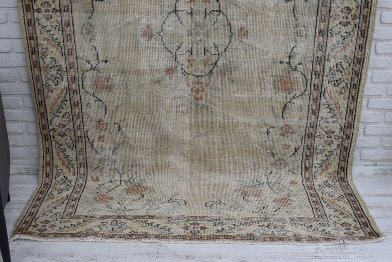 May include: A vintage rug with a beige background and a floral pattern in shades of brown, black, and cream. The rug has a fringed edge.