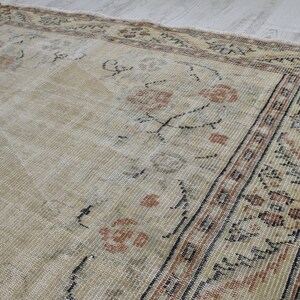 May include: A vintage rug with a cream background and a brown and black border. The rug has a floral pattern in the center and a geometric pattern in the border.