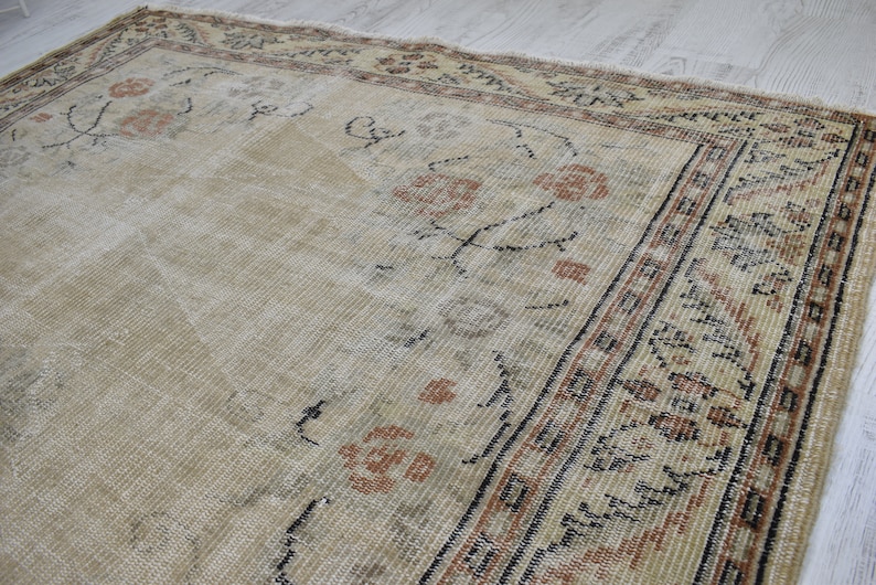 May include: A vintage rug with a cream background and a brown and black border. The rug has a floral pattern in the center and a geometric pattern in the border.