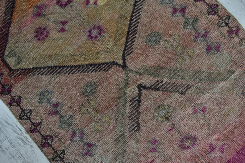 K&ouml;nnte beinhalten: Nahaufnahme eines rosafarbenen und braunen Teppichs mit schwarzem Rand. Der Teppich hat ein florales Design mit kleinen rosa Bl&uuml;ten und gr&uuml;nen Bl&auml;ttern.