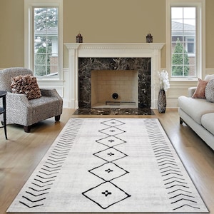 May include: A white and black geometric patterned rug with a diamond design. The rug is laid out on a hardwood floor in front of a fireplace.