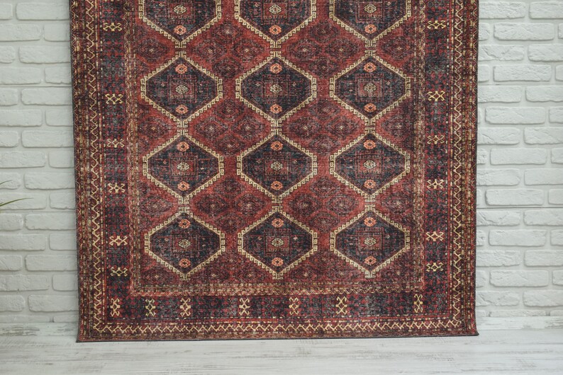 Op de afbeelding: Een rechthoekig tapijt met een geometrisch patroon. Het tapijt heeft een herhalend ontwerp van ruitvormen in tinten rood, bruin en beige. Het tapijt heeft een versleten, vintage uitstraling, met een gedetailleerde rand.
