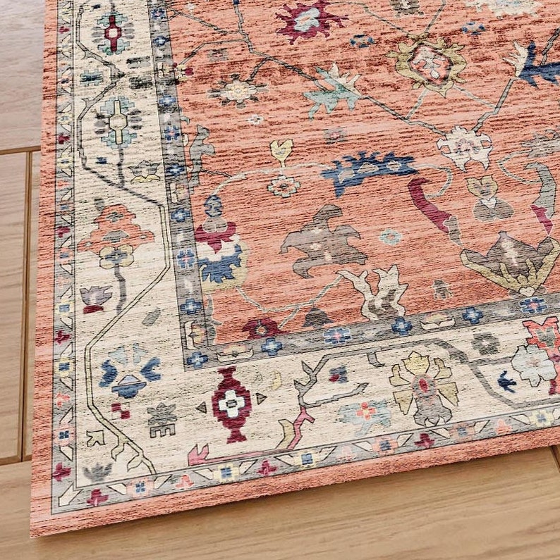 May include: A close-up of a peach-colored rug with a detailed, intricate pattern in shades of blue, red, and white. The rug has a border with a floral design.