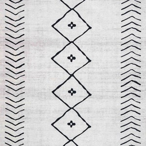 May include: A white rug with a black geometric pattern. The pattern features a series of diamonds with a plus sign in the center, and a border of chevron shapes.