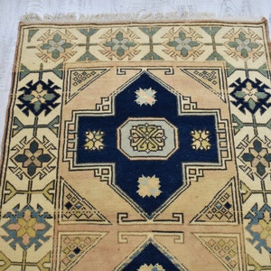 May include: A vintage rug with a cream background and a navy blue center. The rug has a geometric pattern with floral motifs in shades of green, blue, and beige.