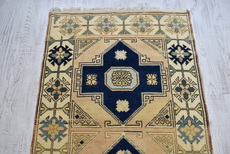 May include: A vintage rug with a cream background and a navy blue center. The rug has a geometric pattern with floral motifs in shades of green, blue, and beige.