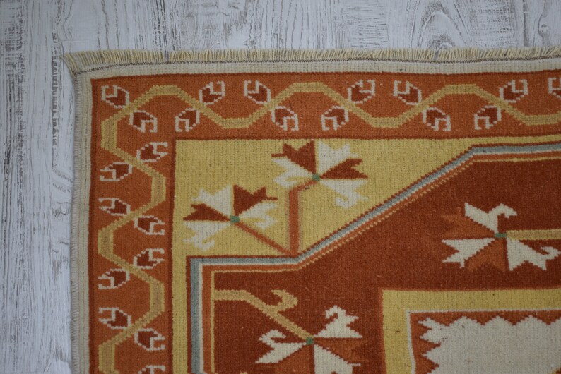 Puede incluir: Primer plano de una alfombra tejida con un patr&oacute;n geom&eacute;trico en tonos naranja, amarillo y blanco. La alfombra tiene un borde con flecos.