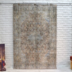 May include: A vintage-style rug with a brown, blue, and beige color scheme. The rug has a geometric pattern with intricate details. The rug is hanging on a white brick wall.