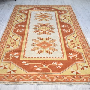 Puede incluir: Una alfombra beige y naranja con un dise&ntilde;o floral. La alfombra tiene un borde de flecos.