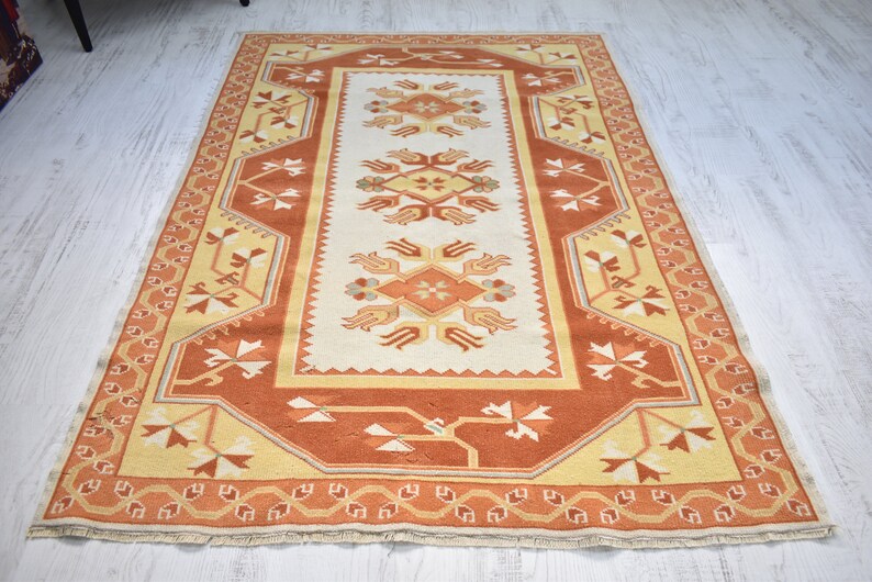 Puede incluir: Una alfombra beige y naranja con un dise&ntilde;o floral. La alfombra tiene un borde de flecos.